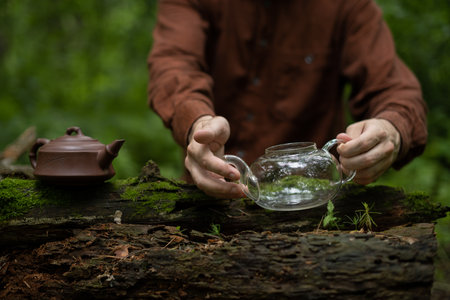 Cropped view of man holding glass cha hai near clay teapot on wooden log with mossの写真素材