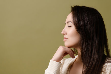 Profile of young Asian woman touching chin isolated on green