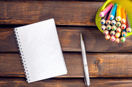 Notepad, pen and colored pencils against the dark boards.の写真素材