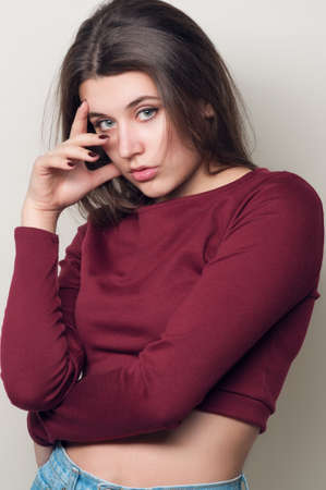 Beautiful young woman. Young girl. Girl in a red top and jeans boyfriends. Beauty portrait.  Girl portrait on a gray background. Toned imageの写真素材