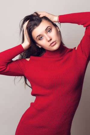 Beautiful young woman. Young girl. Girl in red knitted dress. Beauty portrait.  Girl portrait on a gray background. Toned imageの写真素材