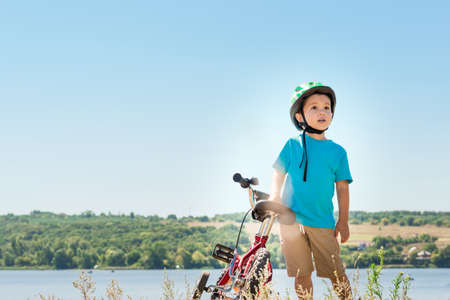 Child riding a bicycle. Child with a bicycle on the river bank. Kid in a helmet riding a bike in the forest. Beautiful baby. Toned image.の写真素材