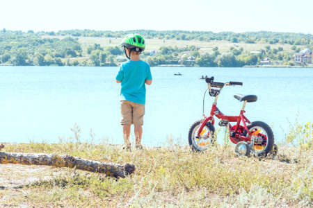 Kid with a bicycle near the river. Child with his beloved bike. Kid in a helmet stands next to bicycle. Beautiful baby. Toned image.の写真素材