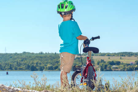 Kid with a bicycle near the river. Child with his beloved bike. Kid in a helmet stands next to bicycle. Beautiful baby. Toned image.の写真素材