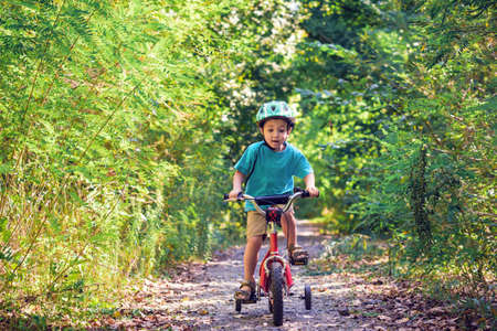 Child riding a bicycle. Kid in a helmet riding a bike in the forest. Beautiful baby. Toned image.の写真素材