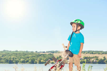Kid helmet bicycle . Sun shines brightly. Child riding a bicycle. Child with a bicycle on the river bank. Beautiful baby. Toned image.の写真素材