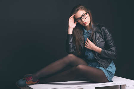 Beautiful young girl. Glasses, denim overalls, a black leather jacket. Sexy girl. Trendy toning...