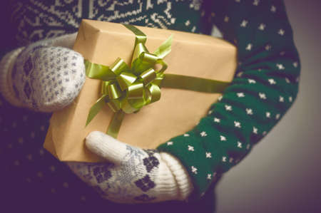 Girl holds in hands Christmas present. Christmas background. Gifts for men. Knitted mittens. Knitted dress. Box with gifts. Merry Christmas. Toned image.の写真素材