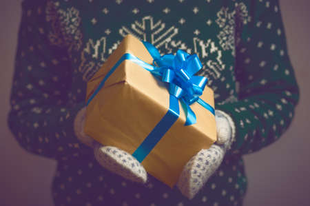 Girl holds in hands Christmas present. Christmas background. Gifts for men. Knitted mittens. Knitted dress. Box with gifts. Merry Christmas. Toned image.の写真素材