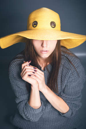 Beautiful girl in yellow hat on a gray background. Sneakers, jeans, sweater. Girl without makeup. Toned image.の写真素材