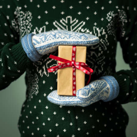 Christmas background. Girl is holding a Christmas present. Gifts for men. Merry Christmas. Gift for a girl. Sweater with Christmas ornament. Knitted dress. Box with gifts. Image in a dark key.の写真素材
