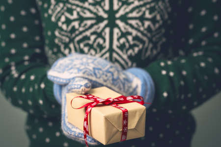 Christmas background. A girl in a New Year's sweater holds a present. Gifts for men. Merry Christmas. Gift for a girl. Sweater with Christmas ornament. Knitted dress. Box with gifts. Toned image.の写真素材
