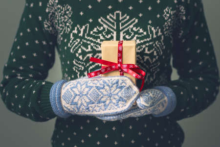 Christmas background. A girl in a New Year's sweater holds a present. Gifts for men. Merry Christmas. Gift for a girl. Sweater with Christmas ornament. Knitted dress. Box with gifts. Toned image.の写真素材