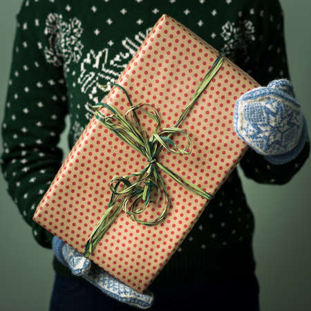 Christmas background. Girl is holding a Christmas present. Gifts for men. Merry Christmas. Gift for a girl. Sweater with Christmas ornament. Knitted dress. Box with gifts. Image in a dark key.の写真素材
