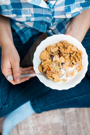 Girl with a plate of cereal. Flakes from whole wheat with dried fruits. Healthy eating concept. A girl in jeans and a plaid shirt. Proper nutrition. Healthy food.の写真素材