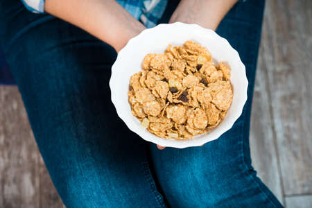 Girl with a plate of cereal. Flakes from whole wheat with dried fruits. Healthy eating concept. A...