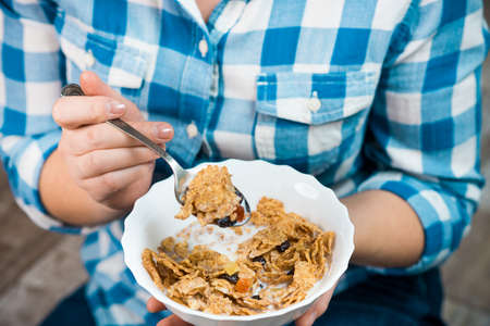 Girl with a plate of cereal. Flakes from whole wheat with dried fruits. Healthy eating concept. A...
