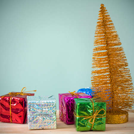 Christmas background. A small gold Christmas tree and boxes with gifts on a wooden table. Green...
