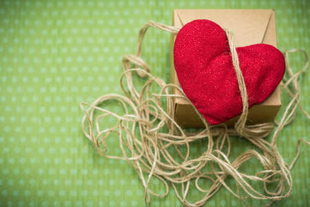 Valentine day. A red heart tied with an old thread to a gift box lies on a green polka dot background. Valentine's Day. Heart pendant. Space for text. Red heart. Eighth of March. International Women's Day.の写真素材