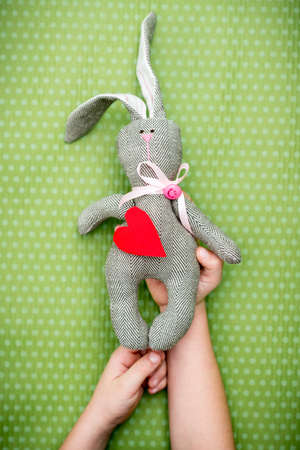 Valentine day. A child holds a rabbit with a red heart in his hand on a green polka dot background....