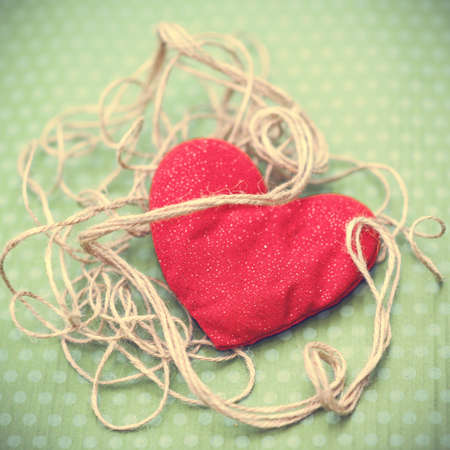 Valentines day. Red heart entwined with vintage threads lies on a beautiful green background. Valentine's Day. Heart pendant. Space for text. Red heart. International Women's Day. Image toned in a fashionable shade.の写真素材