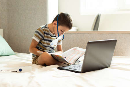 Stay at home quarantine coronavirus pandemic prevention. A child learns home lessons in an oxygen mask with a nibulizer, laptop and a book during quarantine. Prevention epidemic. COVID-19.の写真素材