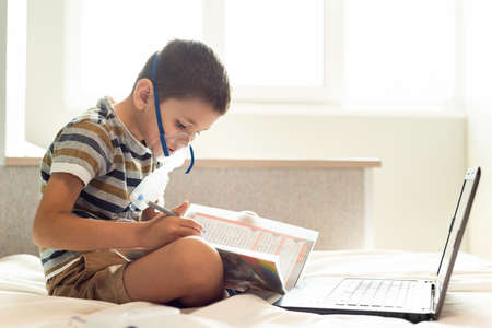 Stay at home quarantine coronavirus pandemic prevention. A child learns home lessons in an oxygen mask with a nibulizer, laptop and a book during quarantine. Prevention epidemic. COVID-19.の写真素材