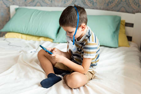 Stay at home quarantine coronavirus pandemic prevention. A child in an oxygen mask with a nibulizer plays on a mobile phone during quarantine. Prevention epidemic. COVID-19.の写真素材