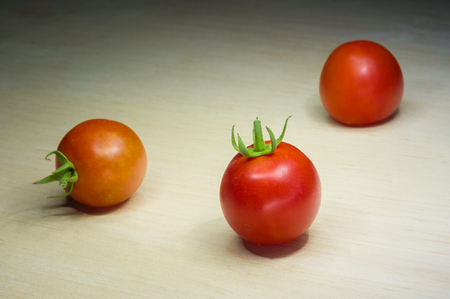Three small red tomatoes on a wooden tableの写真素材