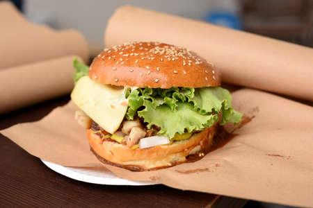 tasty grilled beef burger with lettuce and cheese served on pieces of brown paper on wooden table, street foodの写真素材