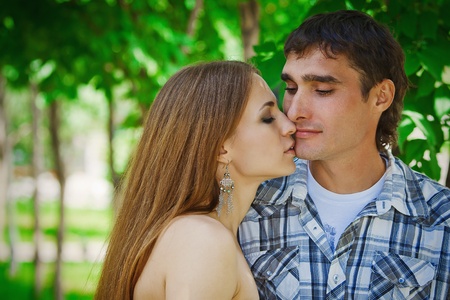 the guy with the girl hugging and kissing in the green foliage of treesの写真素材