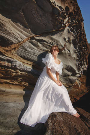 young girl resting on a rocky seashore on a windy dayの写真素材