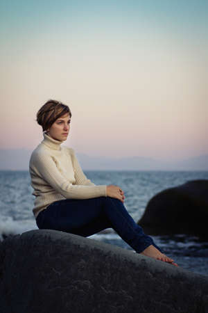 young girl resting on a rocky seashore on a windy dayの写真素材