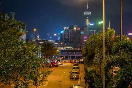Hong Kong, China - 2020: Man Kwong Street from above at night. Street, cars and bus stop, trees. In the distance, skyscrapers in the night illumination.のeditorial素材