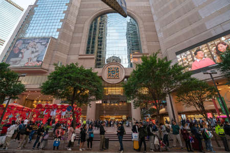 Hong Kong - 2020: people stand on the sidewalk near Times Square mall entrance, beautiful modern building with large windows and unusual clocks, Russell Street.のeditorial素材