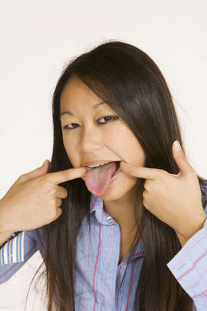 Asian woman making silly faces and sticking out tongueの写真素材