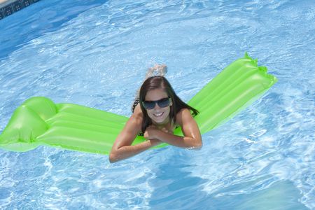 Attractive slim and tanned young lady lying on inflatable sunbed on sunny swimming pool on vacation...