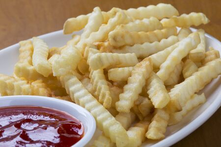 A plate full of delicious crinkle cut style french fries with ketchup