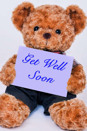 Cute teddy bear holding a purple sign that reads Get Well Soon isolated on a white backgroundの写真素材