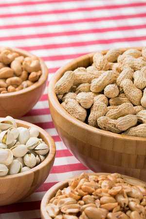 Close up of party bowls of peanuts, almonds, pistachios, and cashews on a red checkered tablecloth