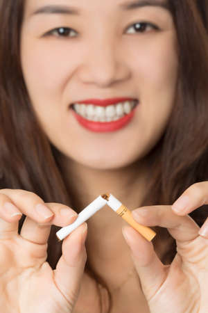 Beautiful Asian woman smiling while breaking a cigarette to quit smoking isolated on a white backgroundの写真素材
