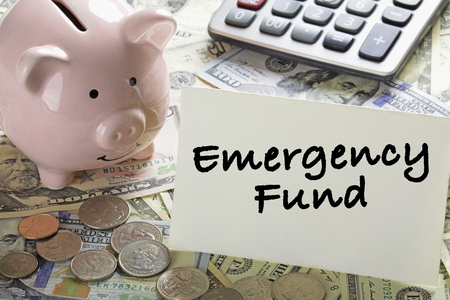 United States bank notes and coins with a calcultor, piggy bank, and a card saying Emergency Fundの写真素材