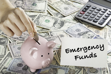 United States bank notes and coins with a calculator, piggy bank, and hand placing coin into piggy bank and a Emergency Funds cardの写真素材