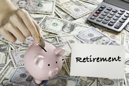 United States bank notes and coins with a calculator, piggy bank, and hand placing coin into piggy bank and a Retirement cardの写真素材