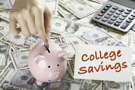 United States bank notes and coins with a calculator, piggy bank, and hand placing coin into piggy bank and a card that says College Savingsの写真素材