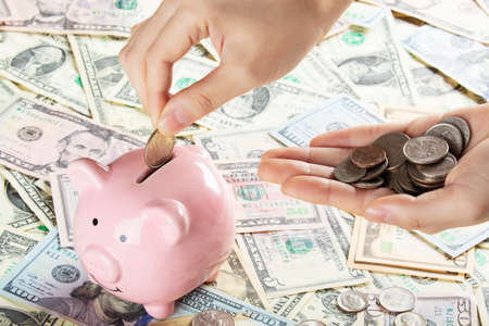 Female hand holding Amicana coins and placing a quarter into a piggy bank isolated on a background...