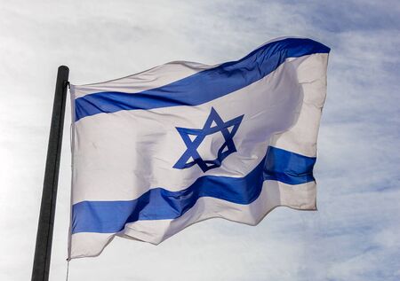 Israel flag flaping in the wind.the flag is flapping and there are blue clouds behind it.