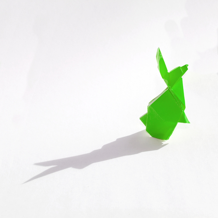 Origami rabbit made of colored paper. the rabbit is standing on a white surface and casts shadow.
It has long pointy ears.の写真素材