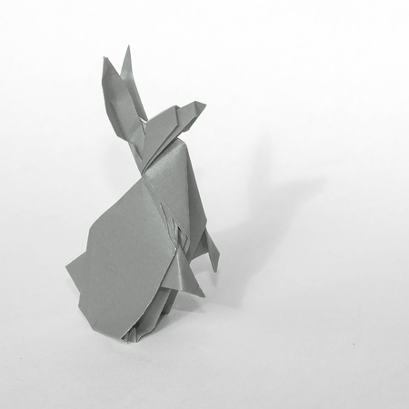 Gray Origami rabbit made of colored paper. the rabbit is standing on a white surface and casts shadow.
It has long pointy ears.の写真素材