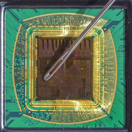 Open computer chip with gold wire connections compared to a needleの写真素材
